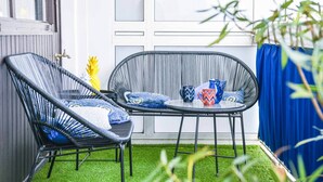 Zwei Korbstühle mit Kissen, ein kleiner Tisch mit einer blauen Tasse und einem dekorativen Gegenstand, und eine Ananas auf der Fensterbank.