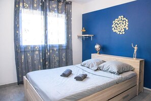 Ein Schlafzimmer mit einem Bett, zwei Kissen, einem Nachttisch mit Lampe, einer Wanddekoration und einem Fenster mit Vorhängen.