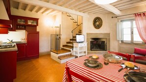 Une cuisine chaleureuse avec des meubles de rangement rouges, une table à manger recouverte d’une nappe à rayures rouges et blanches, et une cheminée.