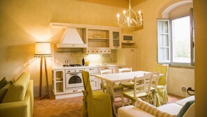 A cozy kitchen with a dining area, featuring a chandelier, white cabinets, and a tiled backsplash. - Farmhouse San Pietro apartment Fern (Castiglion Fibocchi)