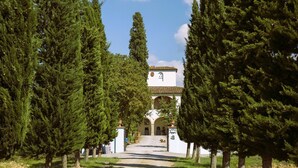 A pathway leading to a building with a white facade and arched entrance, surrounded by tall evergreen trees. - Farmhouse San Pietro apartment Fern (Castiglion Fibocchi)