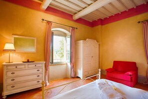 A bedroom with a bed, a dresser, a red chair, a wardrobe, and a window with curtains.