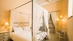 A four-poster bed with white bedding, a nightstand with a lamp, and a chair.