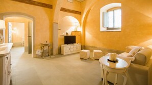 A spacious living area with a sofa, a small round table, and a television on a white cabinet.