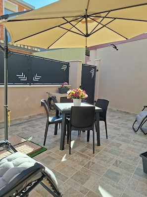A patio with a table, chairs, a wheelchair, a potted plant, and a large umbrella. - Holiday Home Dolia Center (Dolianova)