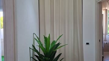 A hallway with a potted plant, a hanging light fixture, and a door leading to another room.