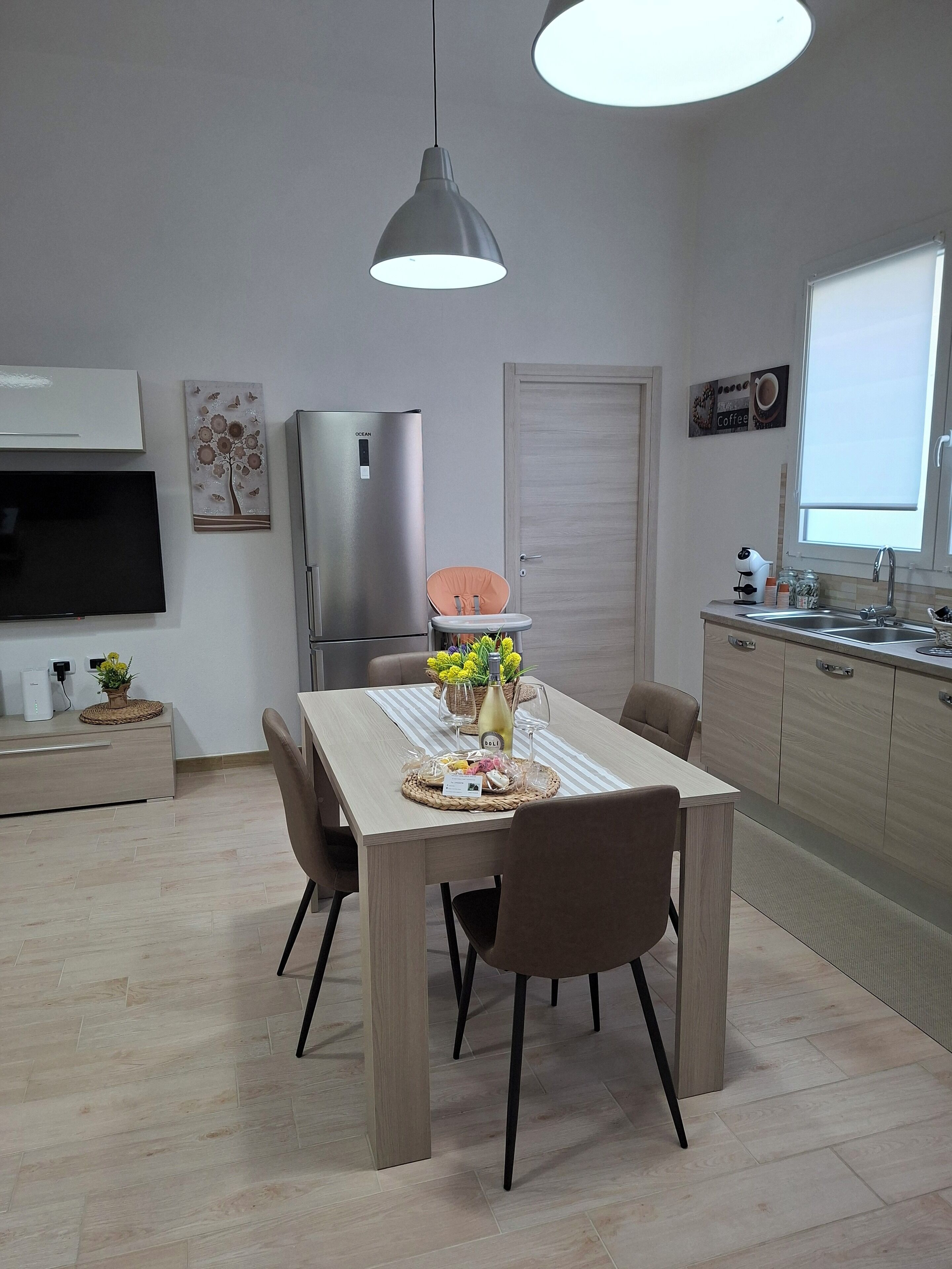 A modern kitchen with a dining area, a refrigerator, a TV, and a window with a view.