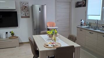 A modern kitchen with a dining area, a refrigerator, a TV, and a window with a view.