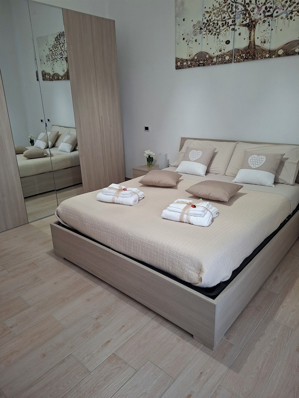 A modern bedroom with a large bed, a wardrobe, and a mirror.