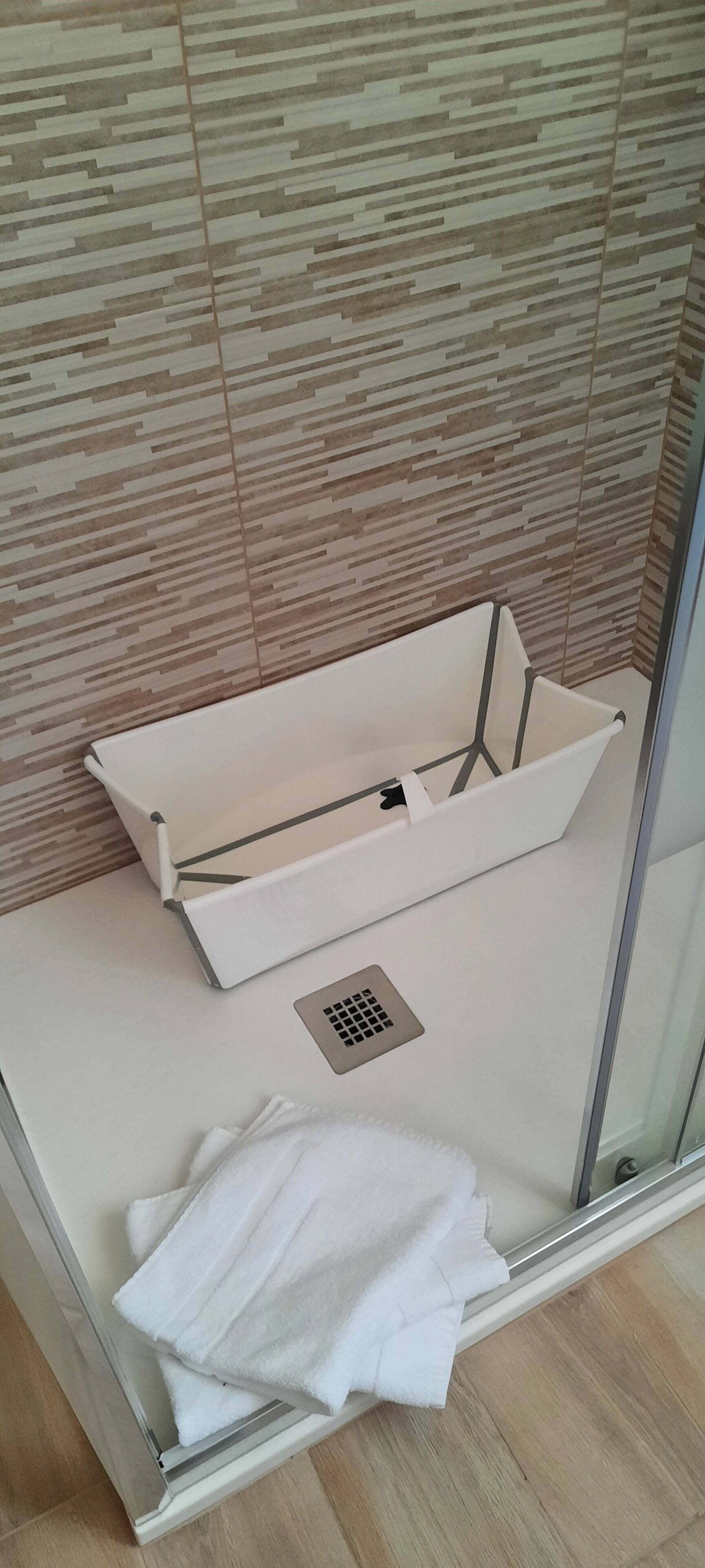 A shower area with a glass door, a white towel, and a showerhead.