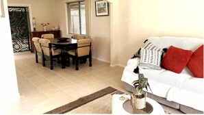 A living room with a sofa, a dining table with chairs, and a potted plant. - Sydney Blue mountain Retreat (Kingswood)