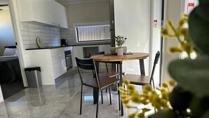 A modern kitchen with white cabinets, a black countertop, and a round wooden table with two chairs. - Sydney Blue mountain Retreat (Kingswood)