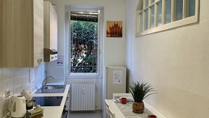 Cocina compacta con ventana, radiador y una pequeña mesa con una planta y una taza roja.