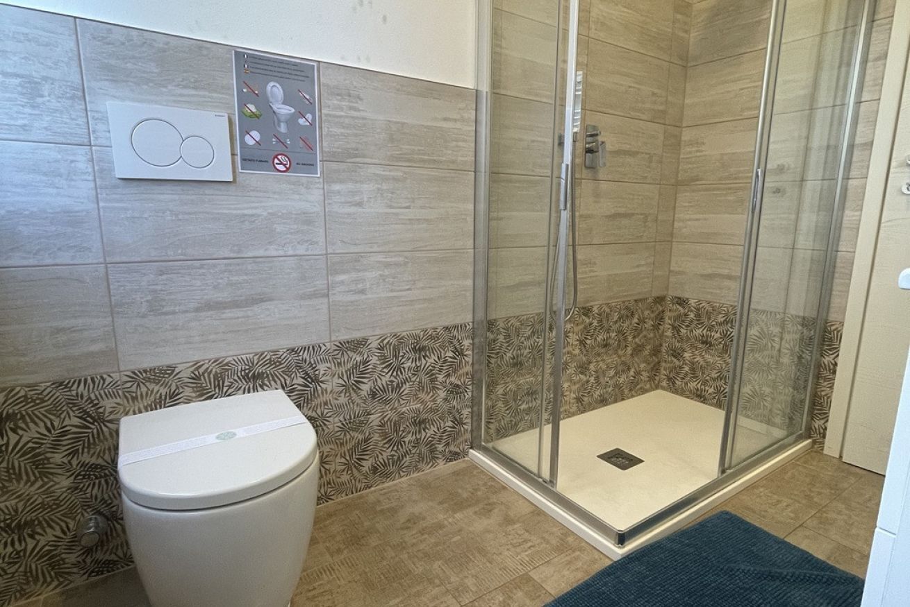Ein Badezimmer mit Toilette, einer Duschkabine mit Glastür, gemusterten Fliesen und einer Bedienkonsole.