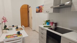 Una cocina moderna con armarios blancos, una estufa negra y una encimera blanca. Hay una pequeña planta en maceta sobre la encimera y una señal roja con texto blanco.