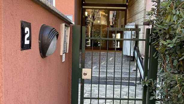 Una entrada protegida por una reja a un edificio, con un letrero con el número '2' en la pared, un buzón y una pequeña planta en maceta a la derecha.