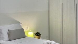 Una cama bien hecha con almohadas, una lámpara de noche y una pequeña planta en maceta.