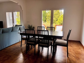A dining area with a table and chairs, a sofa, and a view through a glass door. - Holiday home in the greenest region of Portugal (Gandra)