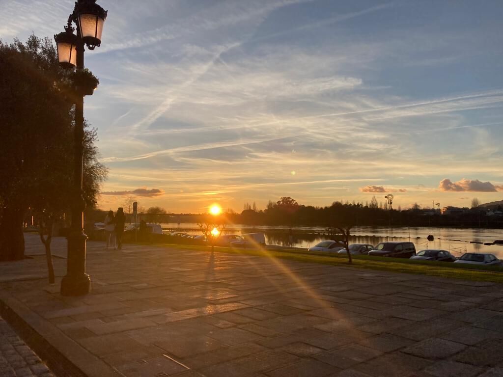 A sunset over a body of water with parked cars and a lamp post.
