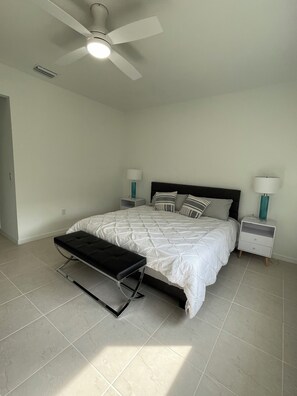 A bedroom with a bed, a bench, two bedside tables with lamps, a ceiling fan, and a light fixture.