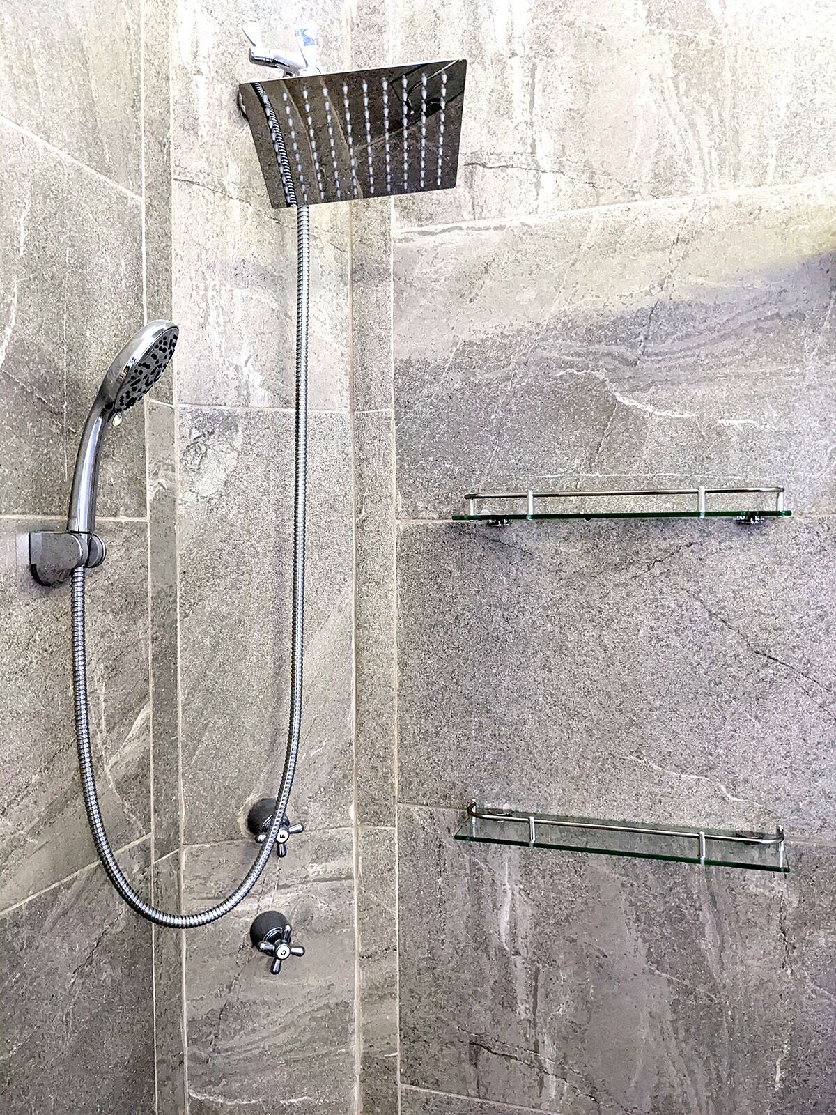 Une douche équipée d’un pommeau de douche à main et d’un pommeau de douche fixe, tous deux fixés sur un mur carrelé.