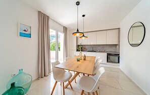 Uma cozinha moderna com armários brancos, uma mesa de jantar de madeira e duas luminárias pendentes.