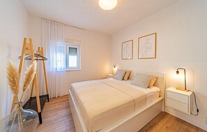 Quarto com cama, mesas de cabeceira, janela com cortinas e decoração nas paredes.
