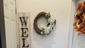 A hallway with a 'WELCOME' sign, a wreath, and a door with a decorative arrangement. - Brighten Your Day Getaway (Rexburg)