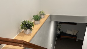 A staircase with a wooden handrail, a small wooden platform with potted plants, and a bed with a white headboard in the background. - Brighten Your Day Getaway (Rexburg)