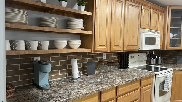 A kitchen with wooden cabinets, a granite countertop, a microwave, and various kitchen items. - Brighten Your Day Getaway (Rexburg)