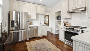 A modern kitchen with white cabinetry, stainless steel appliances, and a wooden floor.