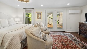 A bedroom with a bed, a sofa, a patterned rug, a dresser, and a door leading to a balcony.