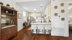 A modern kitchen with white cabinets, a stainless steel refrigerator, and a bar area with white bar stools.