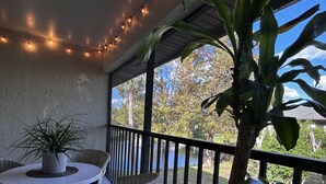 Um espaço ao ar livre coberto com uma mesa redonda e cadeiras de vime, luzes de festa e plantas em vasos.