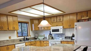 A modern kitchen with wooden cabinets, a central island with bar stools, a hanging light fixture, and a large window. - Cozy Lakeview Cabin outside Jackson Hole
Pallisades Reservoir (Irwin)