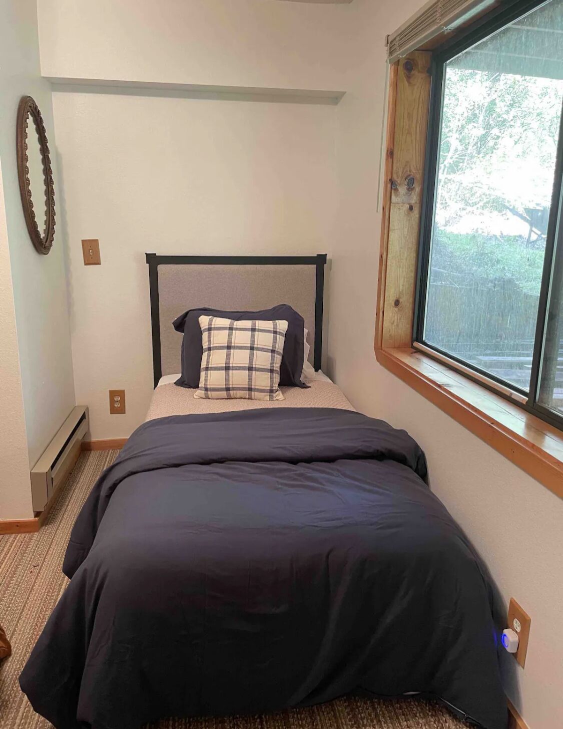 A neatly made bed with a black and white checkered pillow, a dark blue bedspread, and a wooden headboard.