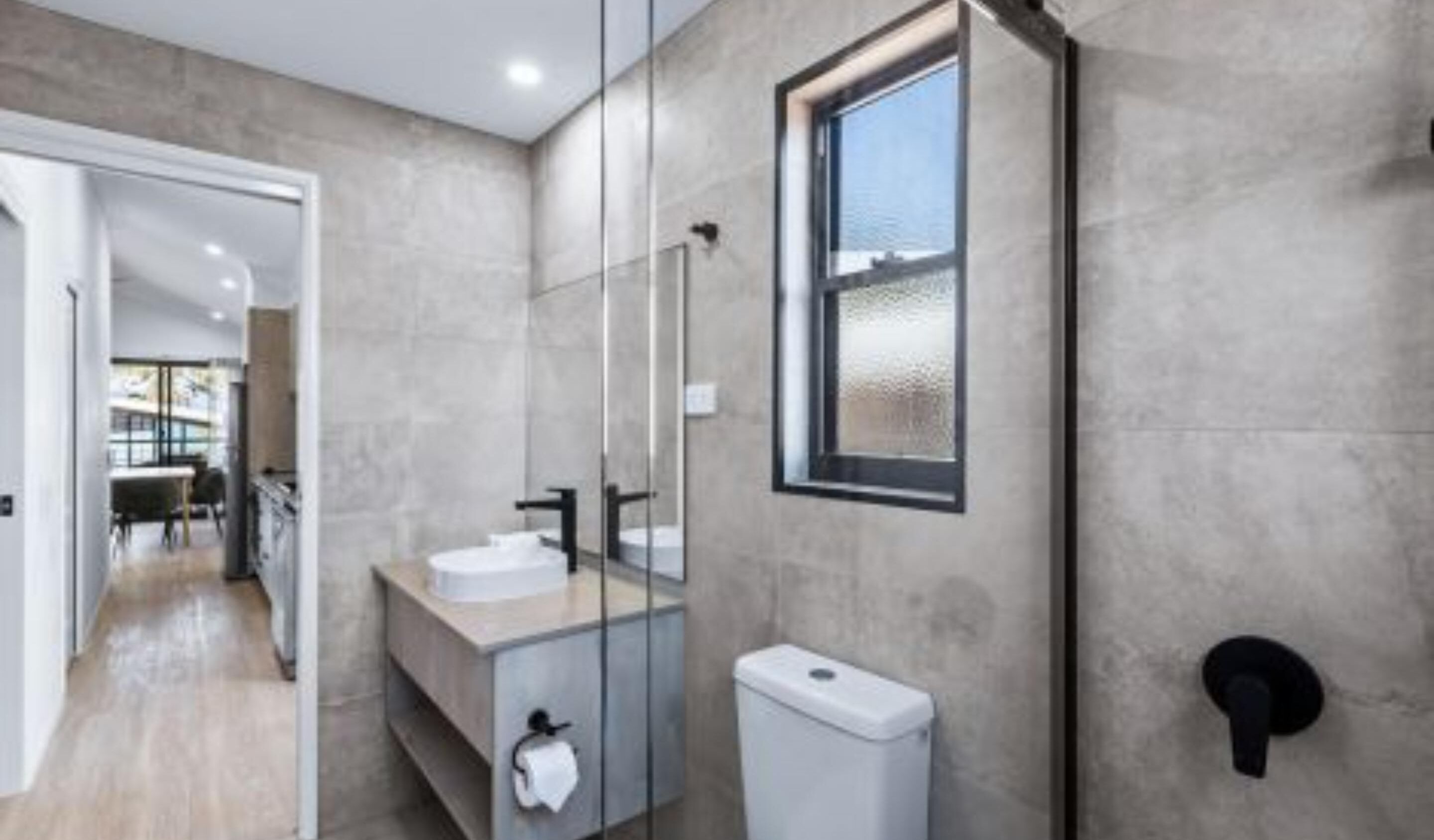 A modern bathroom with a glass shower enclosure, a toilet, and a sink with a mirror.