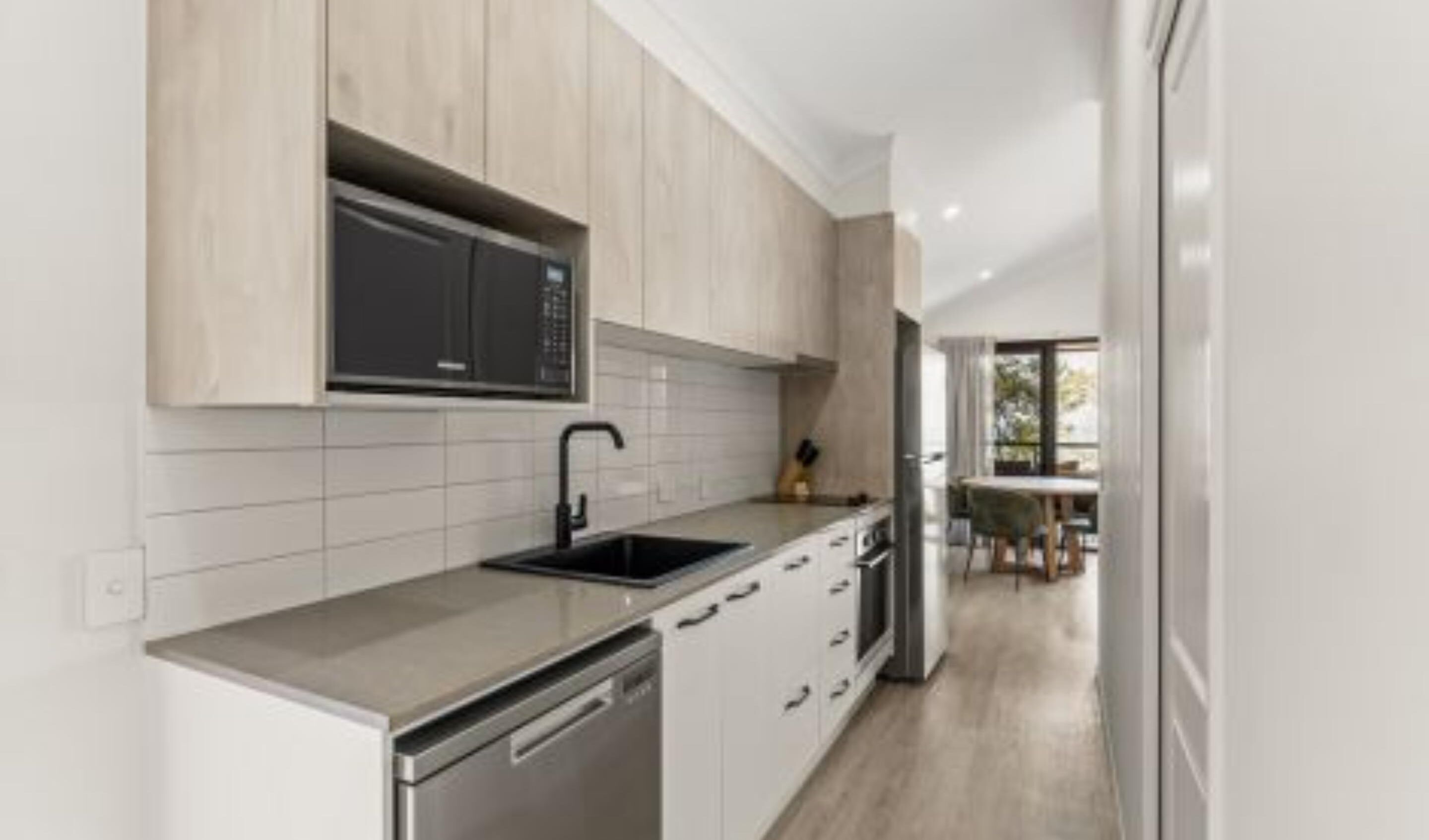 Una cocina moderna con alacenas de madera clara, lavavajillas de acero inoxidable y microondas negro.