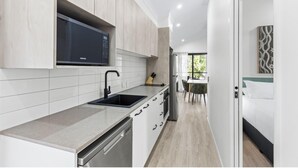 A modern kitchen with white cabinets, a built-in microwave, and a dishwasher. - Discovery Parks - Broome (Broome)