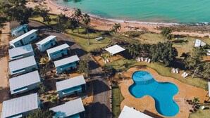 An aerial view of a resort with multiple bungalow-style buildings, a large swimming pool, and a beach. - Discovery Parks - Broome (Broome)