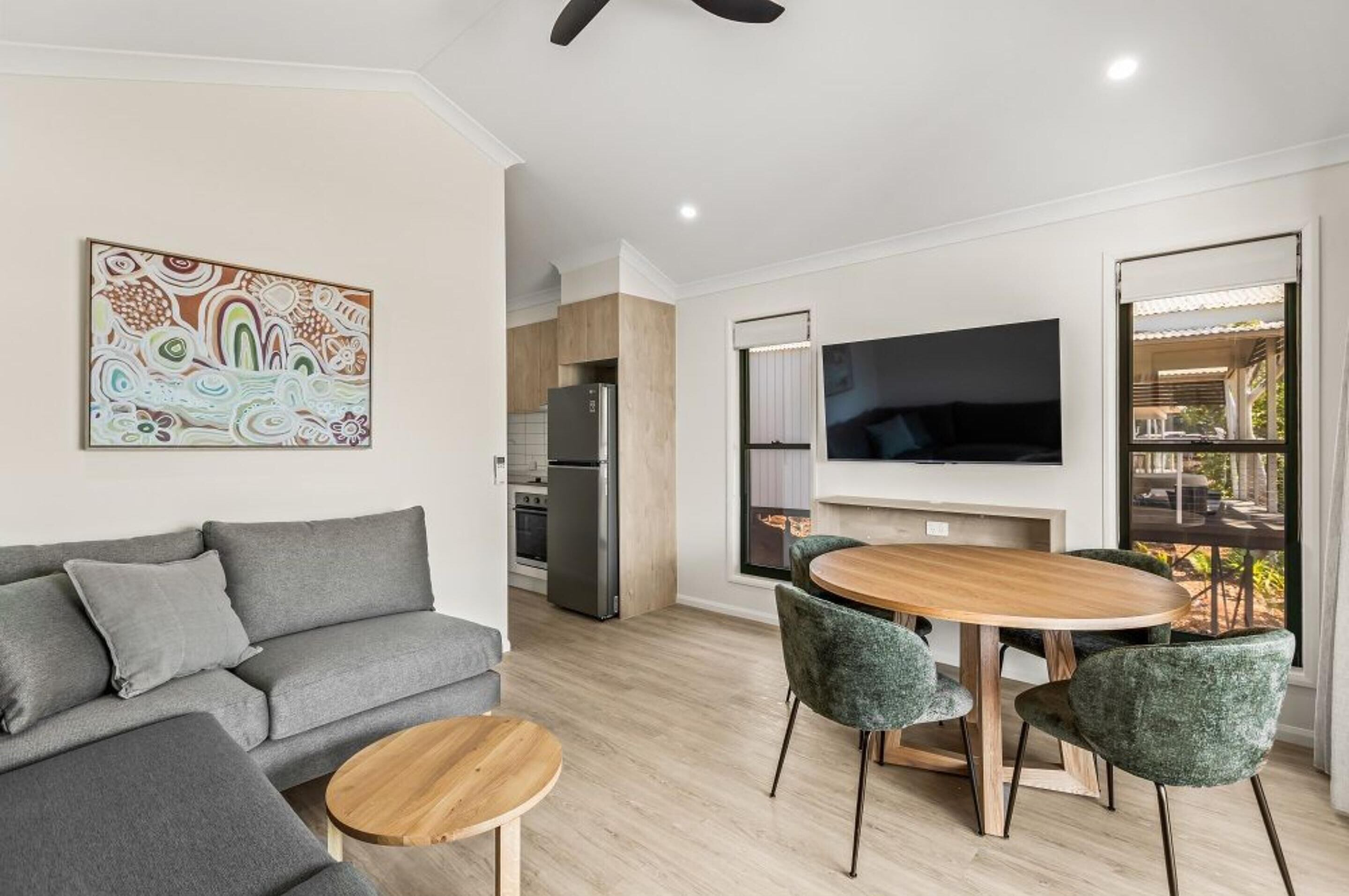Una sala de estar moderna con un sofá gris, una mesa de centro de madera y un comedor con una mesa redonda y sillas verdes.