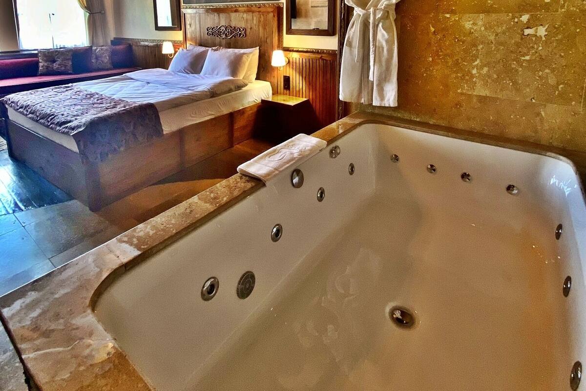 A spacious room with a large bed, a separate sitting area, a bathtub, and a wooden ceiling.
