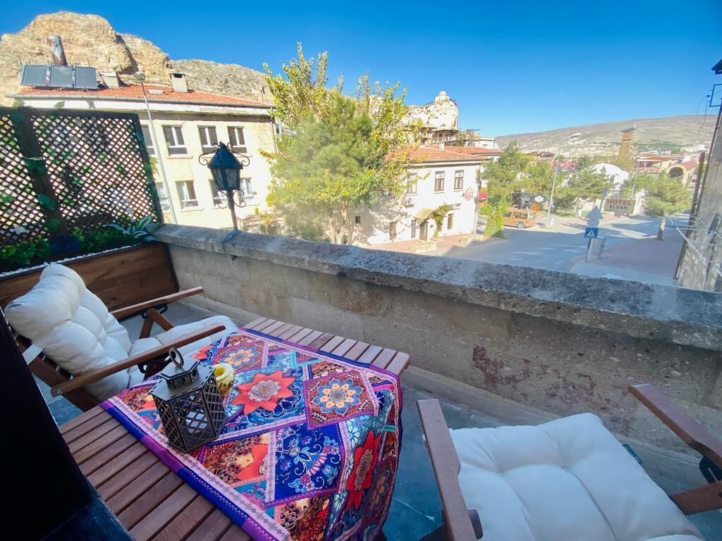 A balcony with a view of a town, a table with a colorful tablecloth, and a chair.