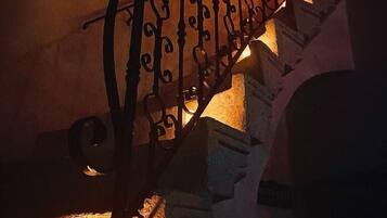 Una escalera con barandillas metálicas ornamentadas y una vela encendida al pie.