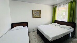 Een hotelkamer met twee enkele bedden, een schilderij aan de muur en een raam met groene gordijnen.