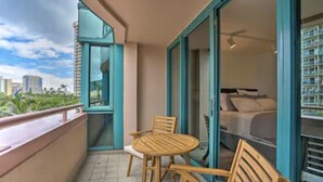 Un balcon avec une table ronde en bois et des chaises, un lit avec un matelas et des oreillers blancs, et une vue sur le panorama de la ville.