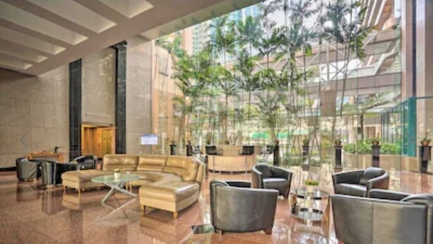 Un hall d’entrée spacieux au design moderne, comprenant un grand espace salon avec des canapés et des fauteuils, une table basse en verre et un comptoir d’accueil.