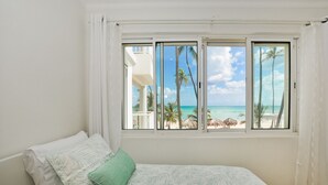 Ein Schlafzimmer mit Bett, Blick auf den Strand und einem Fenster mit Vorhängen.
