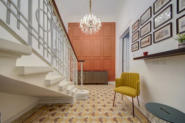 A staircase with white steps and a patterned floor, a yellow chair, a chandelier, and framed pictures on the wall. - Traditional Corner Townhouse for rent. Ideal for Groups or Families! (Bormla)