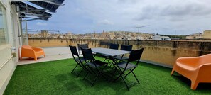 A rooftop terrace with artificial grass, a table with chairs, and a view of a cityscape. - Traditional Corner Townhouse for rent. Ideal for Groups or Families! (Bormla)